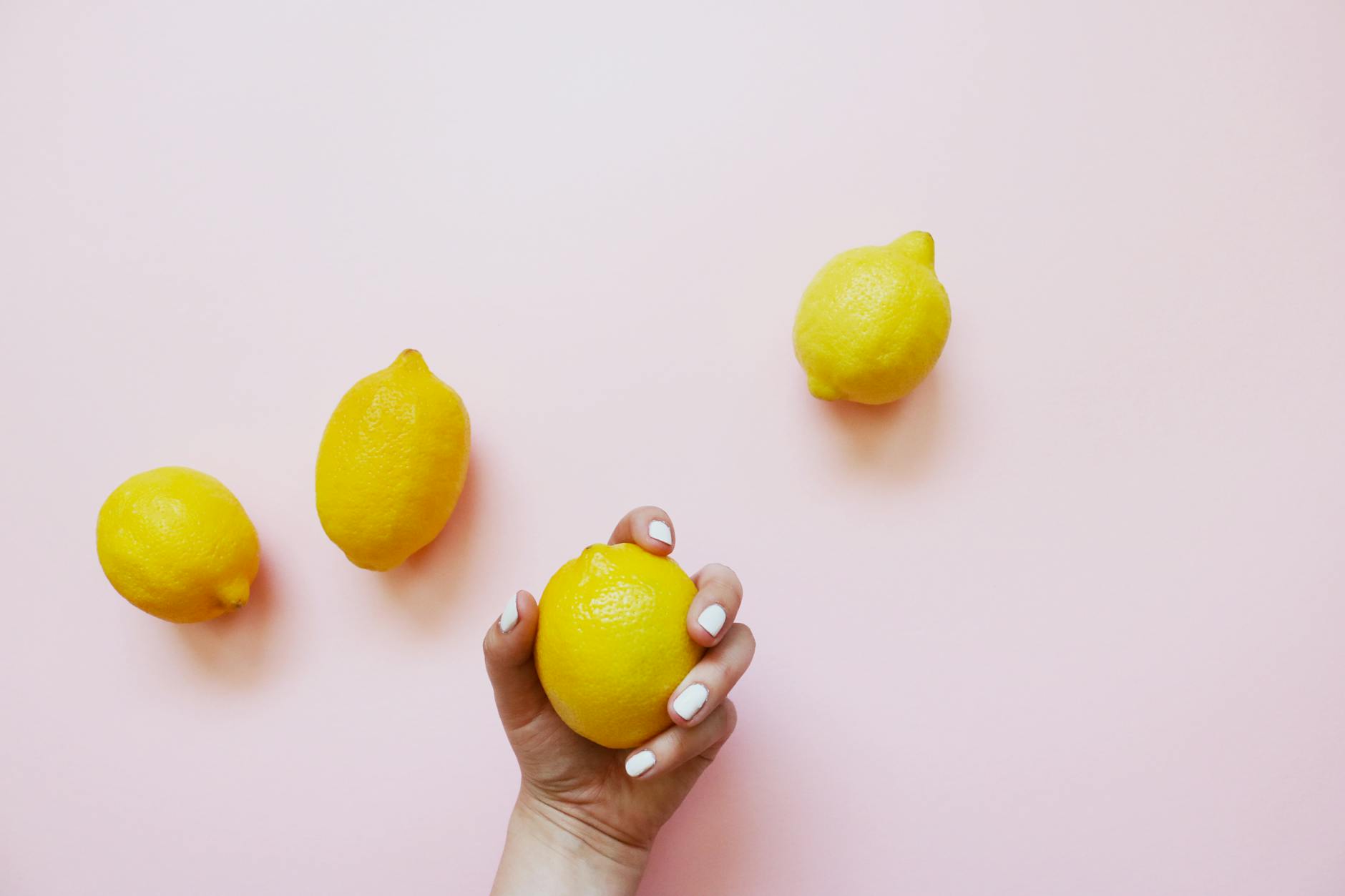 A hand holding a fresh lemon on a soft pink background, symbolizing renewal and gentle self-care during healing