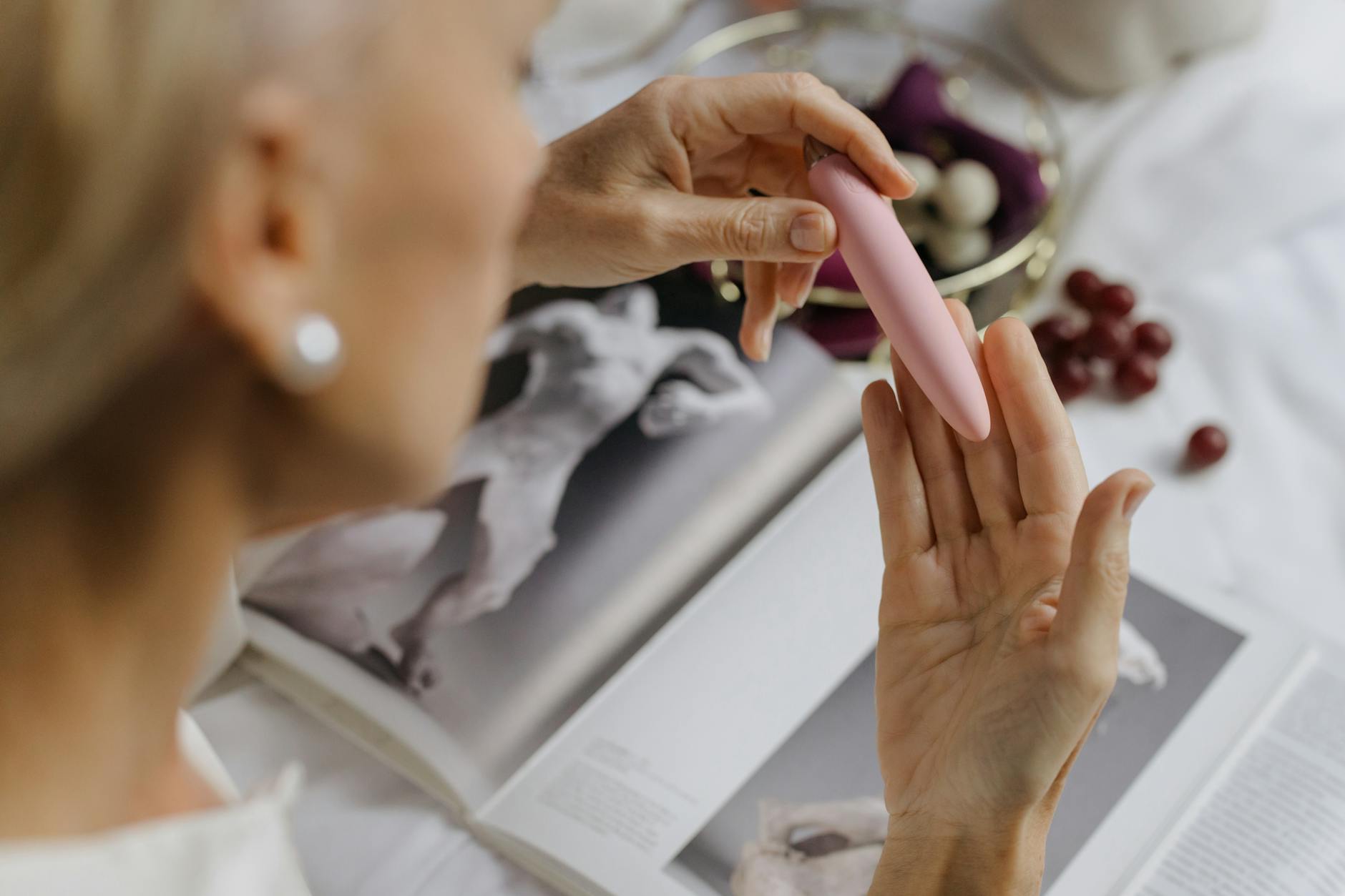 Close-up of a woman holding a pink vibrator with art books in the background, emphasizing intimate and personal self-discovery.